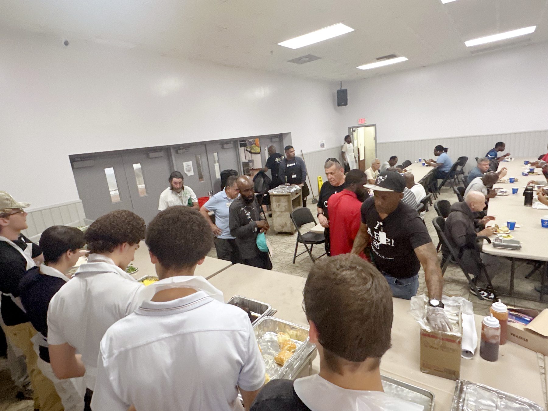 Guests seated at long tables eating while Giving Grill volunteers serve from the front of the hall