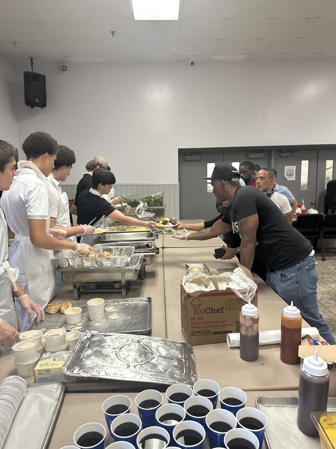 A Giving Grill volunteer passing a full plate across the serving table to a guest reaching for it