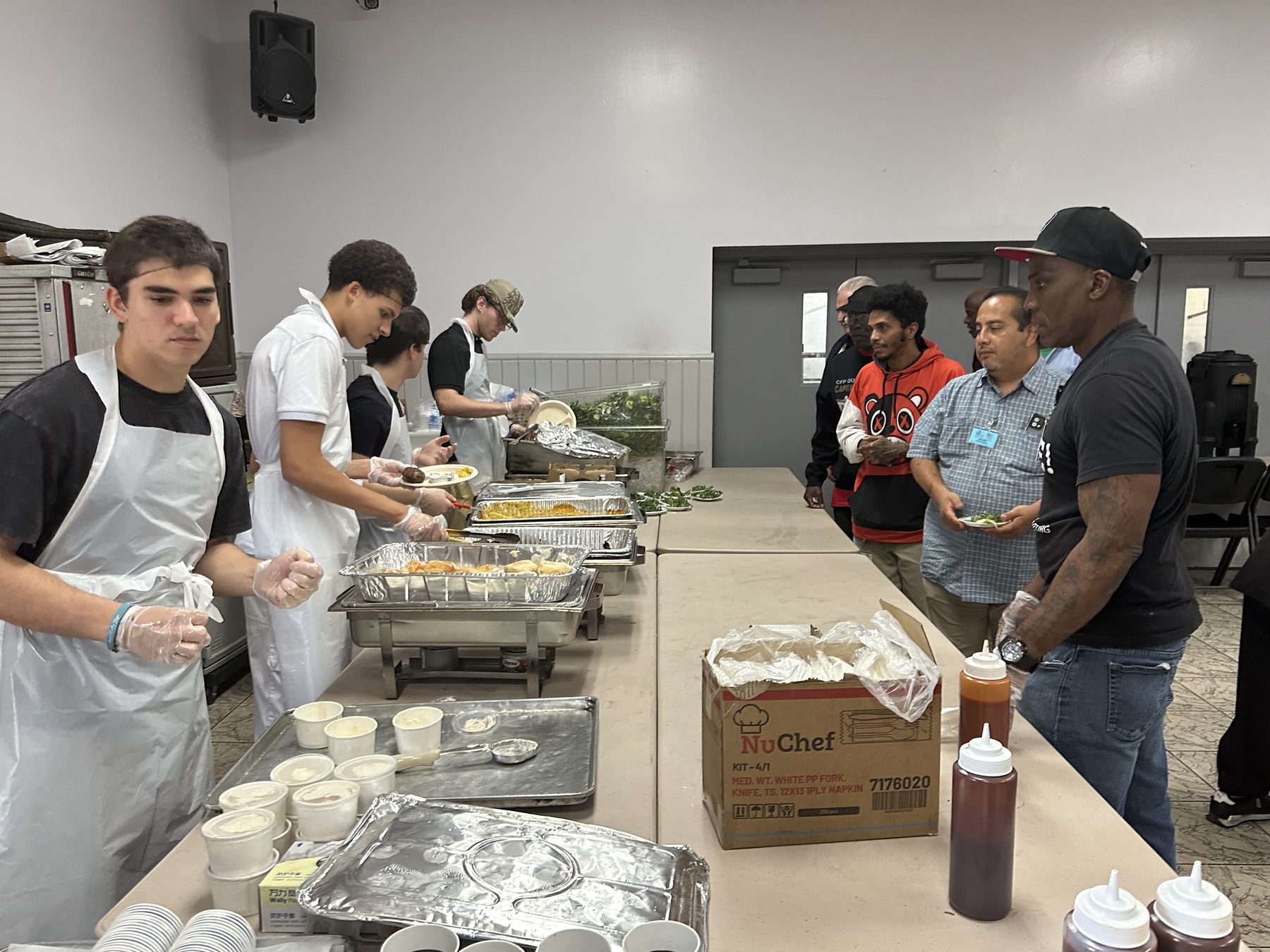 Giving Grill volunteers plating hot food along a serving line as guests wait with their plates